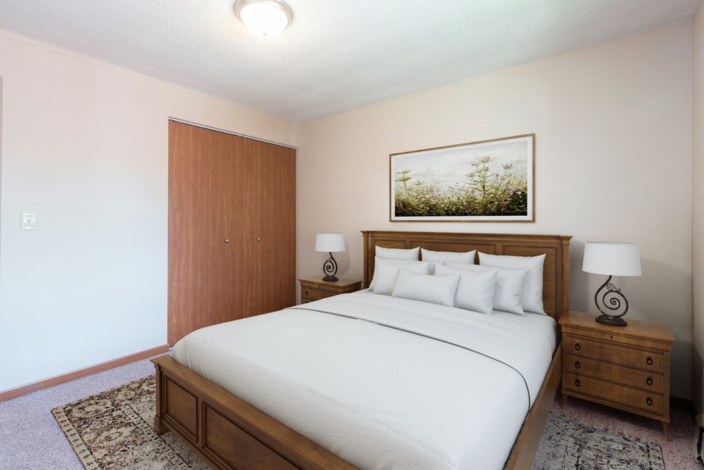 A bedroom with a large bed, a wooden headboard, and a painting above the bed. Bismarck, ND Parkview Arms Apartments