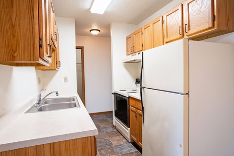 A kitchen with wooden cabinets and a white refrigerator. Fargo, ND Southgate Apartments