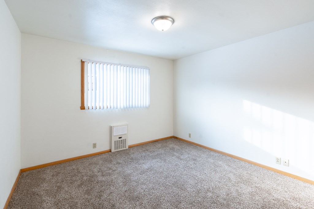 A room with a carpet floor and a window with blinds. Fargo, ND L&R Apartments