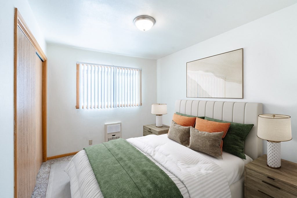 A bedroom with a bed, two lamps, and a mirror. Fargo, ND L&R Apartments