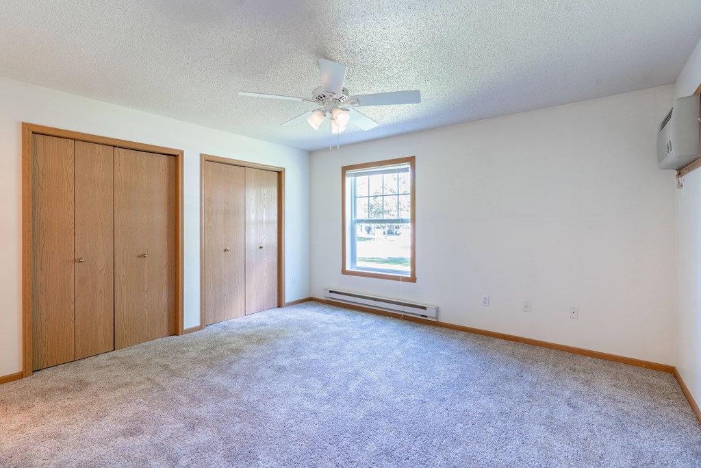 A room with a carpeted floor, a ceiling fan, and a window with blinds. Fargo, ND Stonebridge Apartments