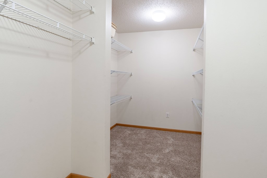 A white closet with a carpeted floor and a light on the ceiling. Fargo, ND Stonebridge Apartments