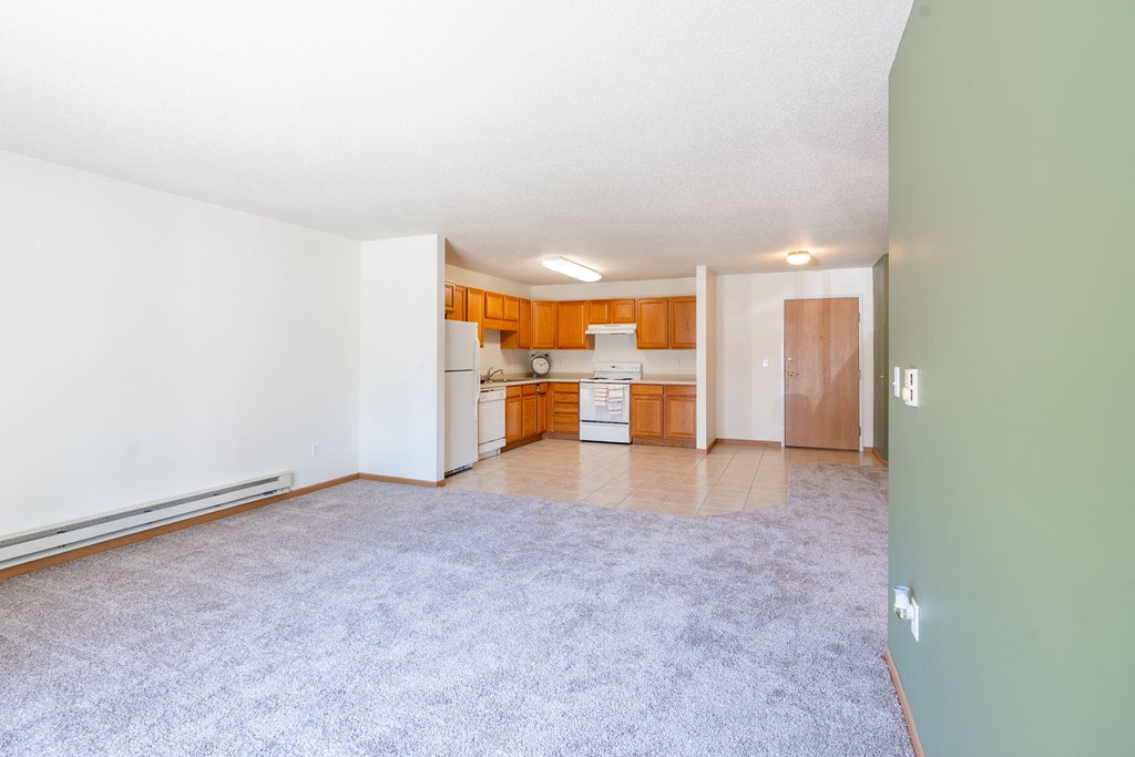 A room with a carpeted floor and a door leading to another room. Fargo, ND Stonebridge Apartments