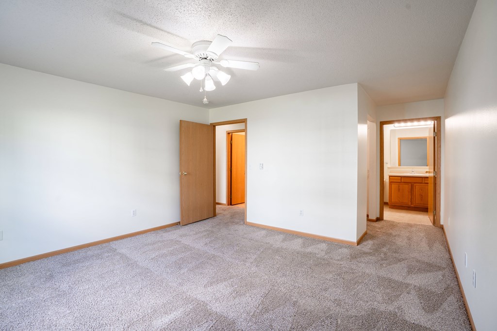 A room with a carpeted floor and a ceiling fan. Fargo, ND Stonebridge Apartments