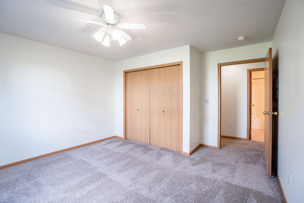 A room with a ceiling fan and carpeted floor. Fargo, ND Stonebridge Apartments