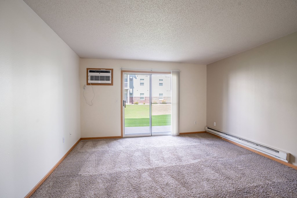 A room with a carpeted floor and a sliding glass door leading to a balcony. Fargo, ND Stonebridge Apartments