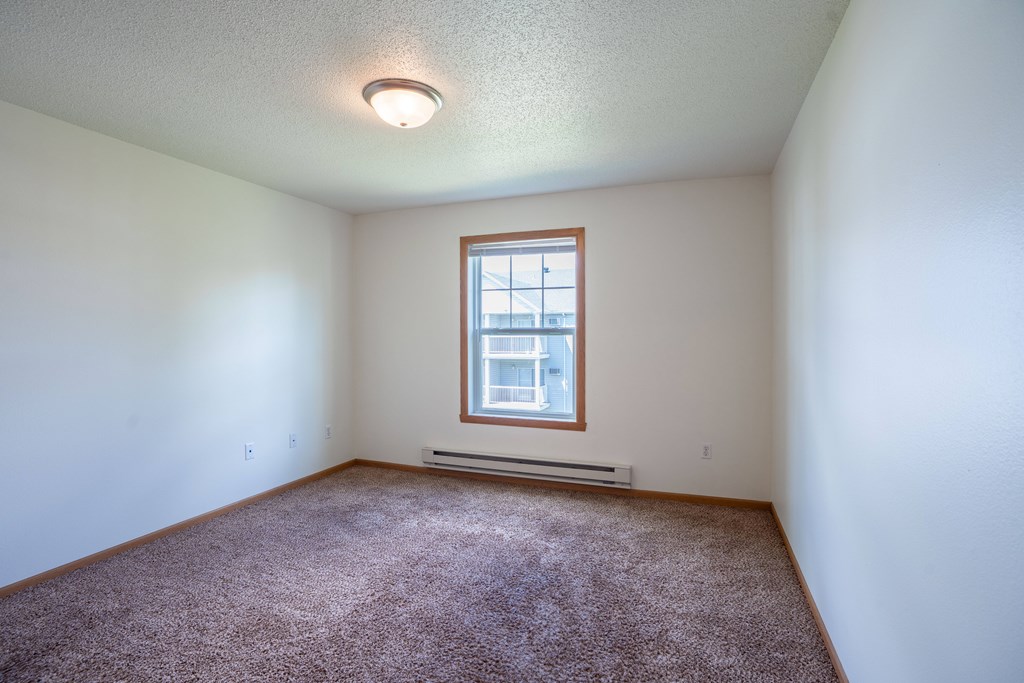 A room with a window and a carpet on the floor. Fargo, ND Stonebridge Apartments