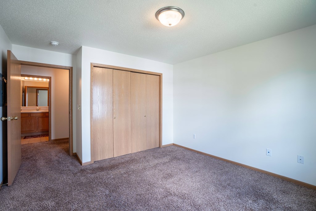 A room with a carpeted floor and a wooden door. Fargo, ND Stonebridge Apartments