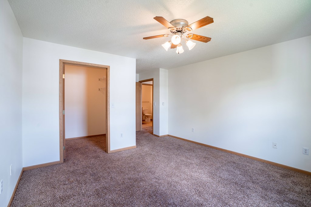 A room with a ceiling fan and carpeted floor. Fargo, ND Stonebridge Apartments