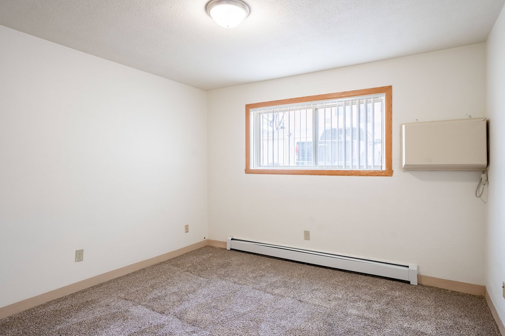 A room with a window and a carpet on the floor. Fargo, ND Islander Apartments