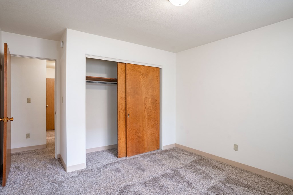 A room with a carpeted floor and a wooden door. Fargo, ND Islander Apartments