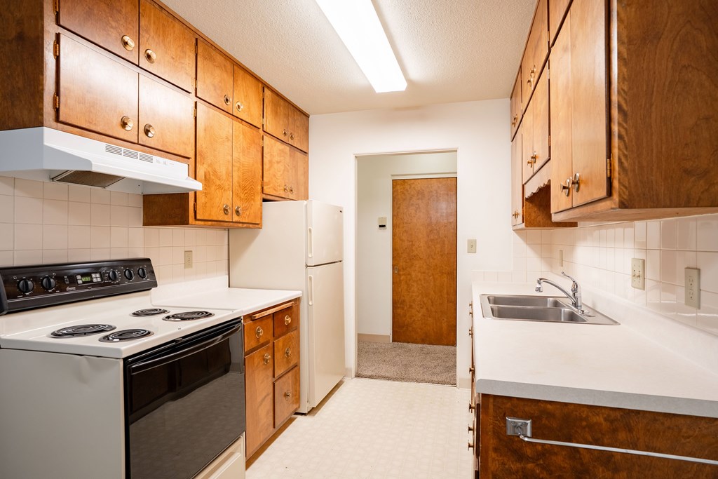 A kitchen with wooden cabinets and a white stove top oven. Fargo, ND Islander Apartments