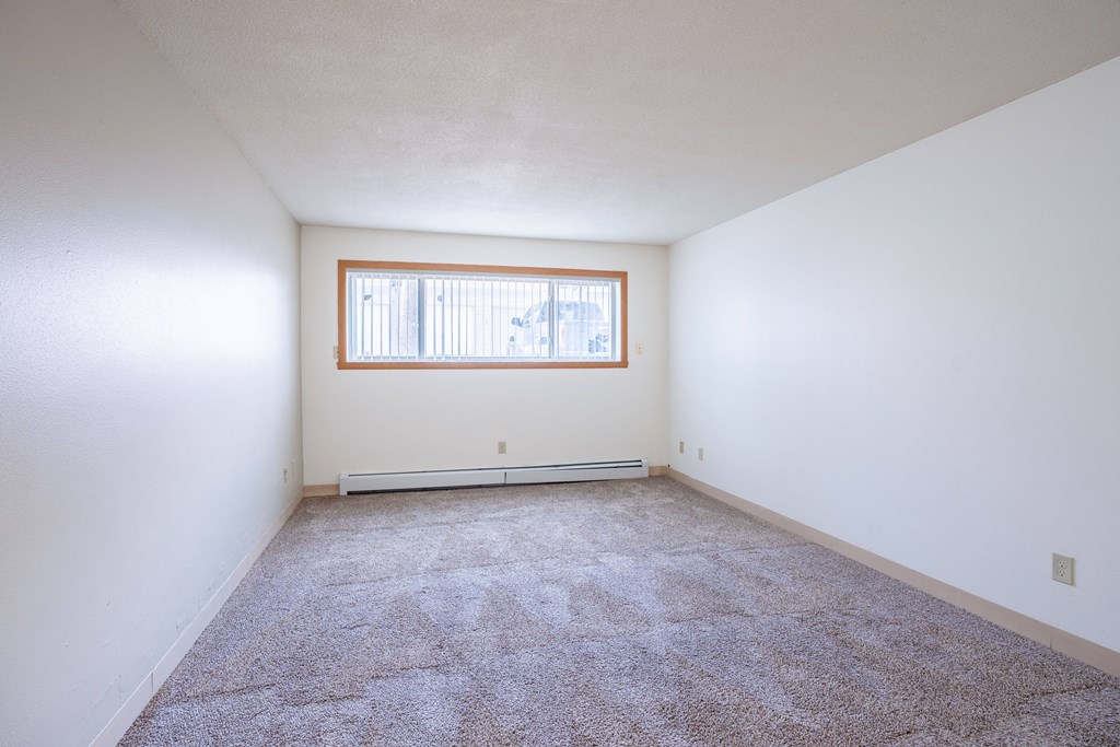 A room with a carpeted floor and a window. Fargo, ND Islander Apartments
