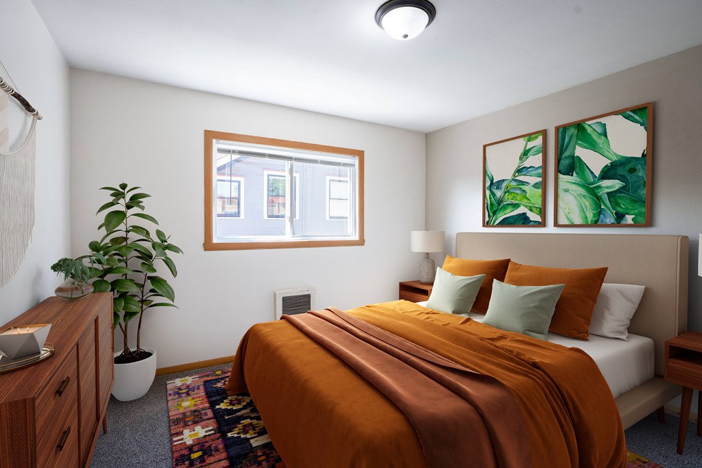 A bedroom with a bed, nightstand, and a potted plant. Fargo, ND L&R Apartments