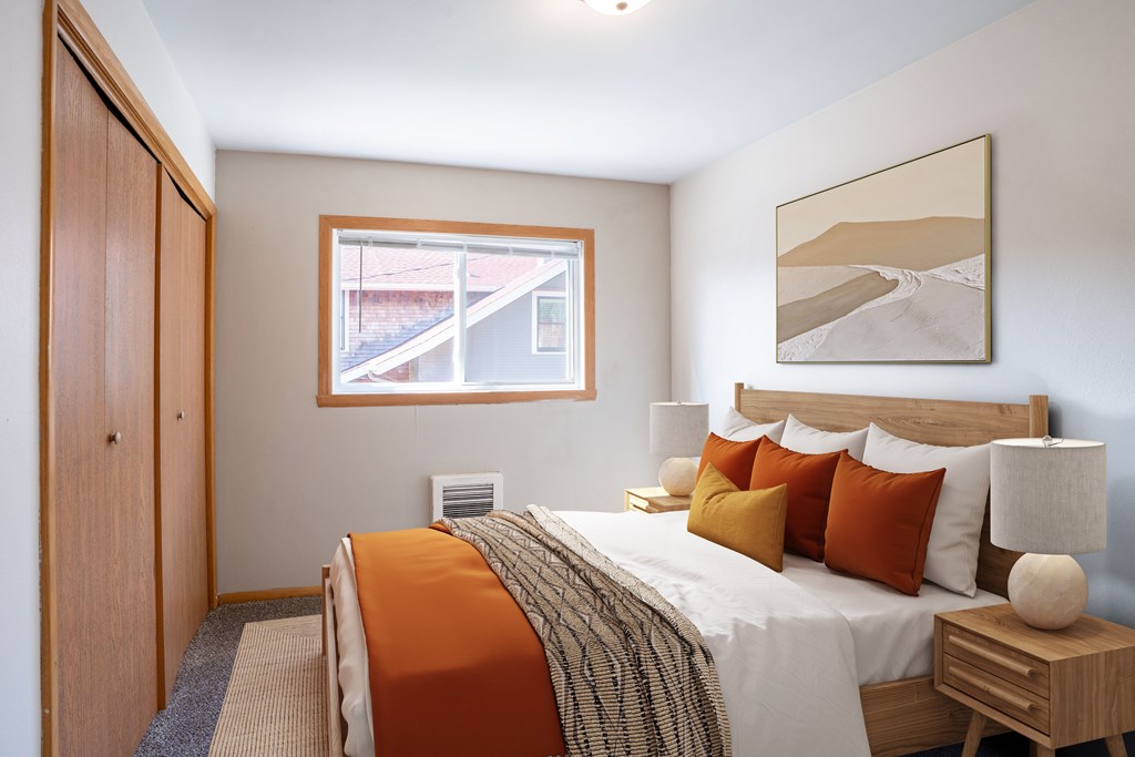 A bedroom with a bed, nightstand, and a painting on the wall. Fargo, ND L&R Apartments