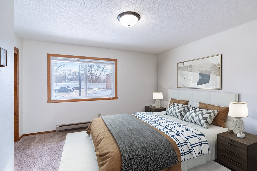 A bedroom with a large bed and a window overlooking a snowy street.  Fargo, ND Carr Apartments