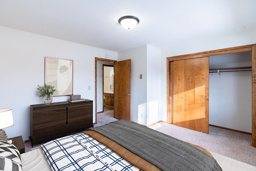 A bedroom with a bed, nightstand, and a painting on the wall. Fargo, ND Carr Apartments