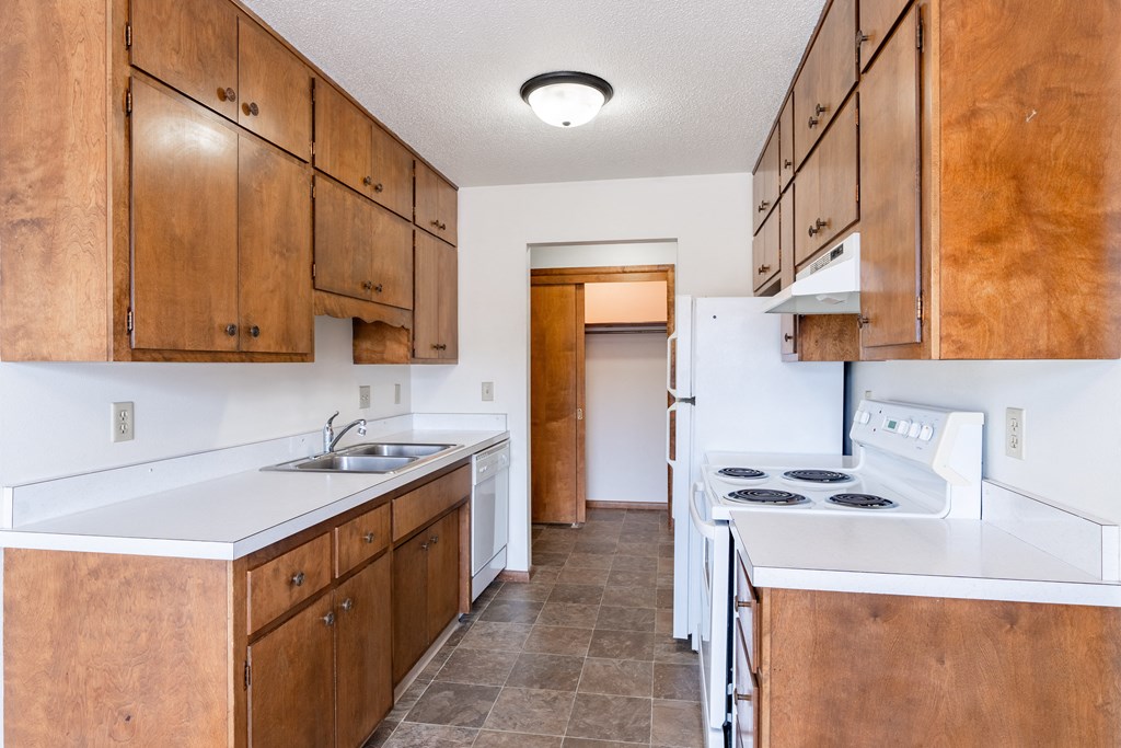 A kitchen with brown cabinets and white appliances. Fargo, ND Carr Apartments