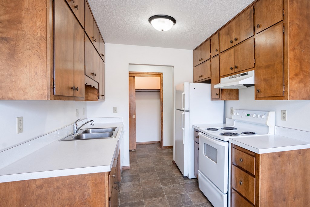 A kitchen with wooden cabinets and a white stove top oven. Fargo, ND Carr Apartments