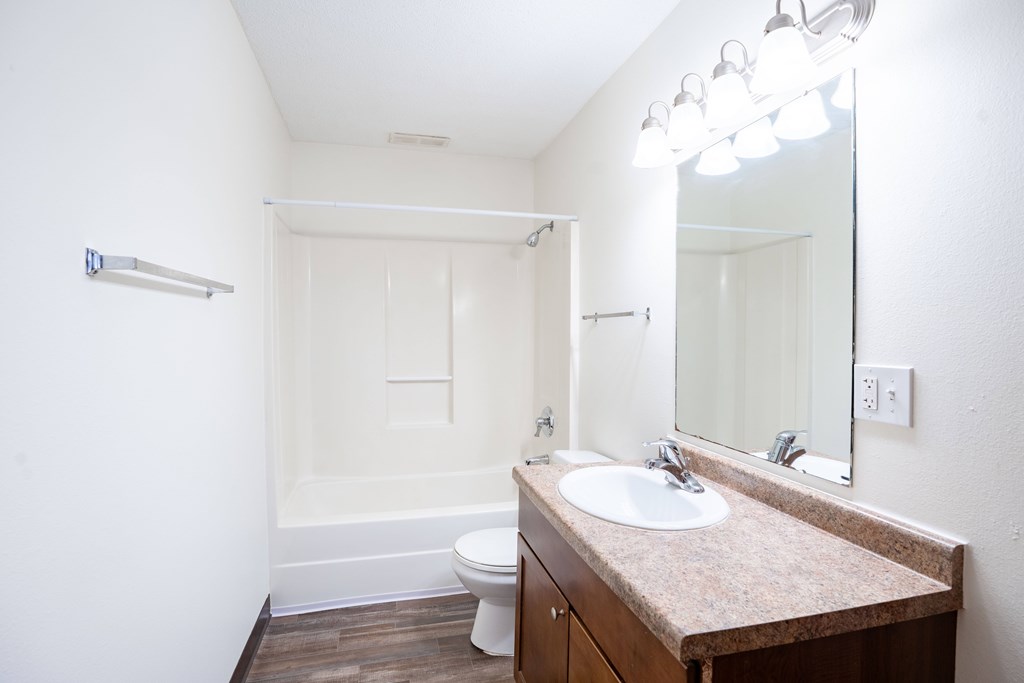 A bathroom with a toilet, sink, mirror, and light fixture. Fargo, ND Westwood Estates