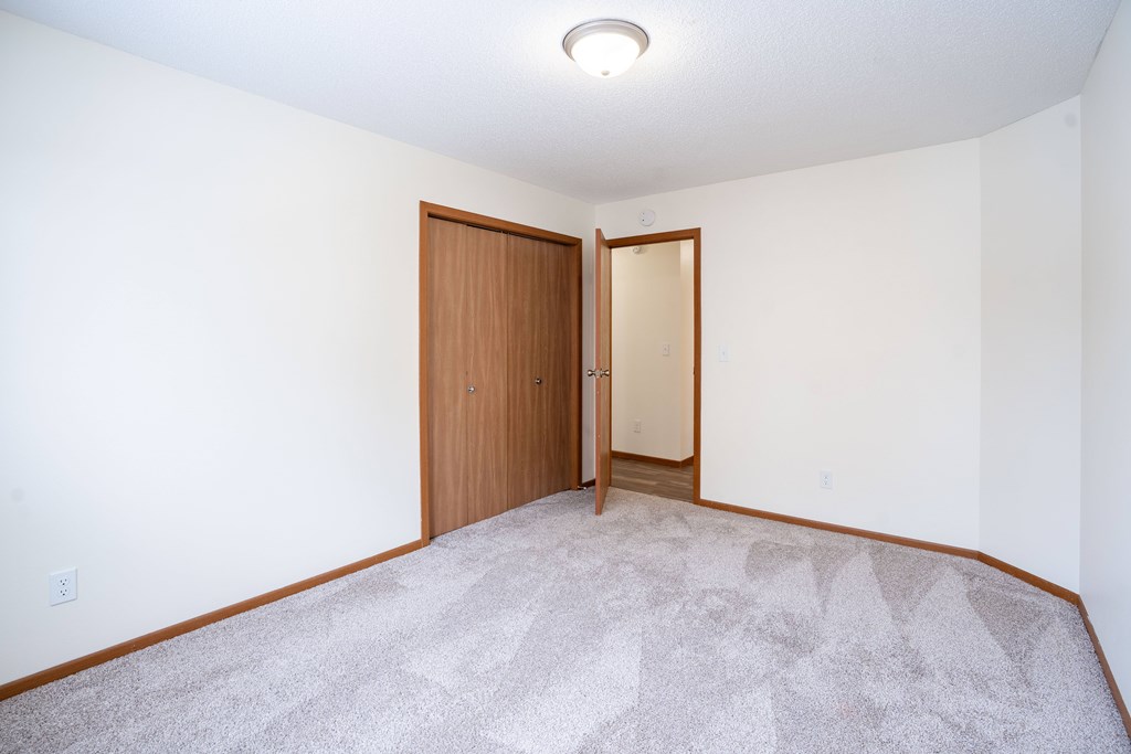 A room with a carpeted floor and a wooden door. Fargo, ND Westwood Estates