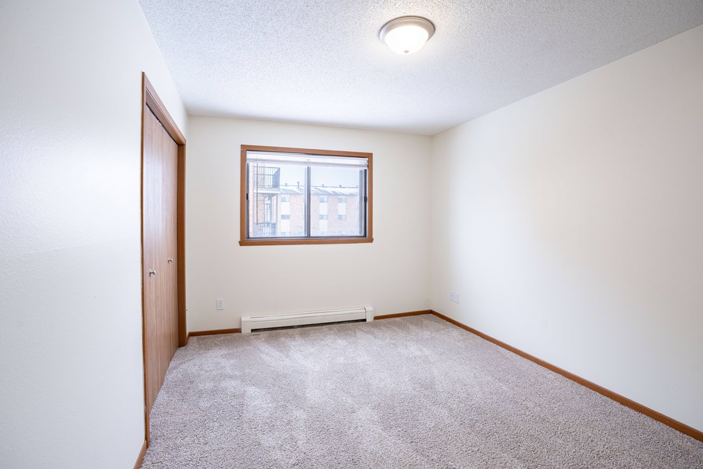 A room with a carpeted floor and a window. Fargo, ND Westwood Estates
