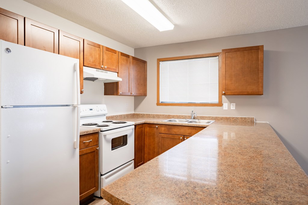 A kitchen with a white refrigerator, brown cabinets, and a granite countertop. Fargo, ND Westwood Estates