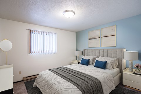 A bedroom with a large bed and a window with blinds. Fargo, ND Countryside Apartments