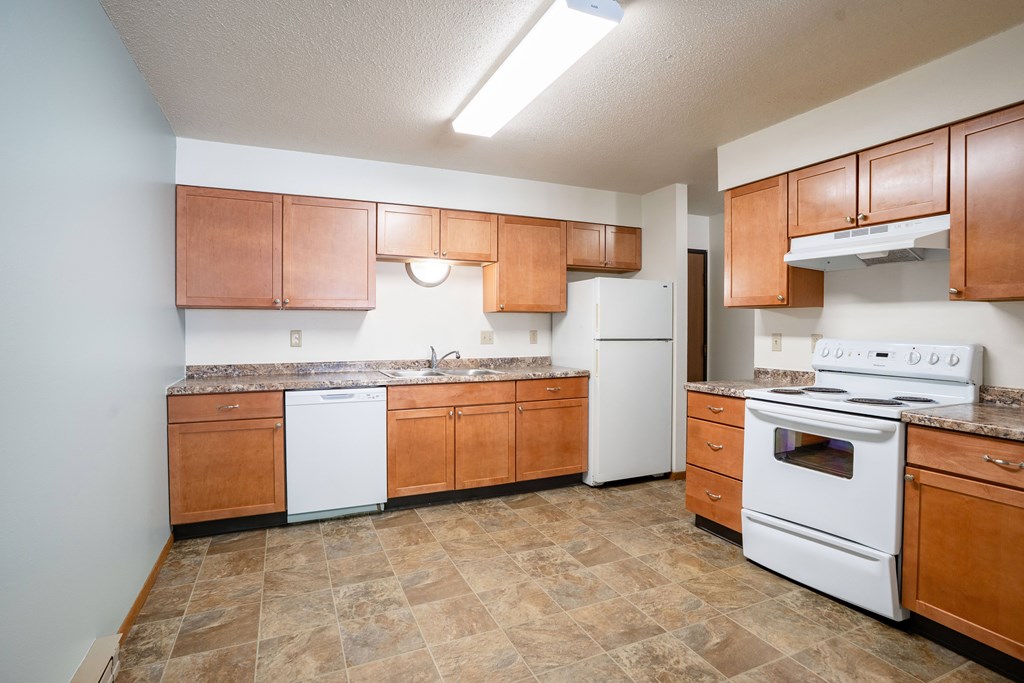 A kitchen with brown cabinets and white appliances. Fargo, ND West Oak Apartments