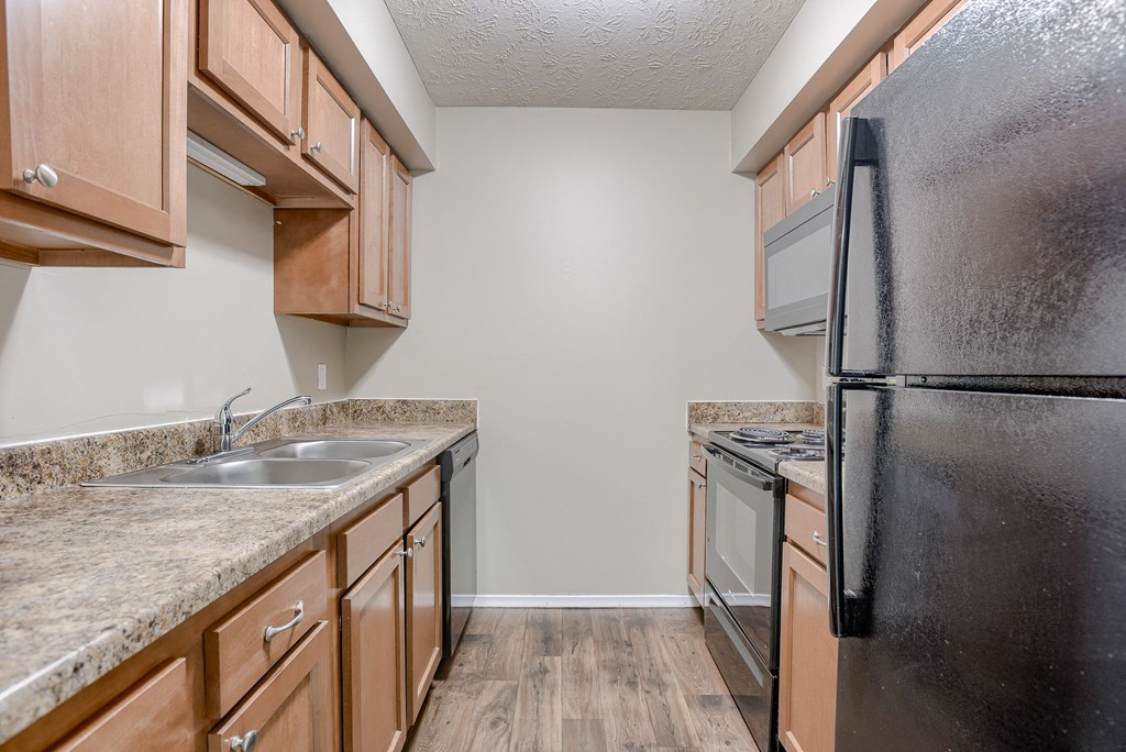 A kitchen with a black refrigerator, brown cabinets, and a granite countertop. Omaha, NE Evergreen Terrace Apartments
