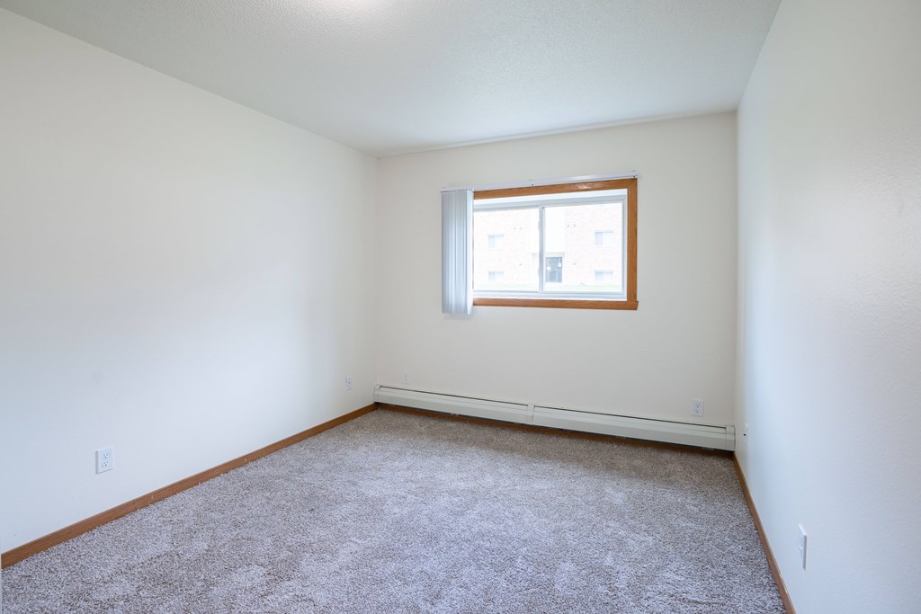 A room with a carpeted floor and a window. Grand Forks, ND Columbia West Apartments
