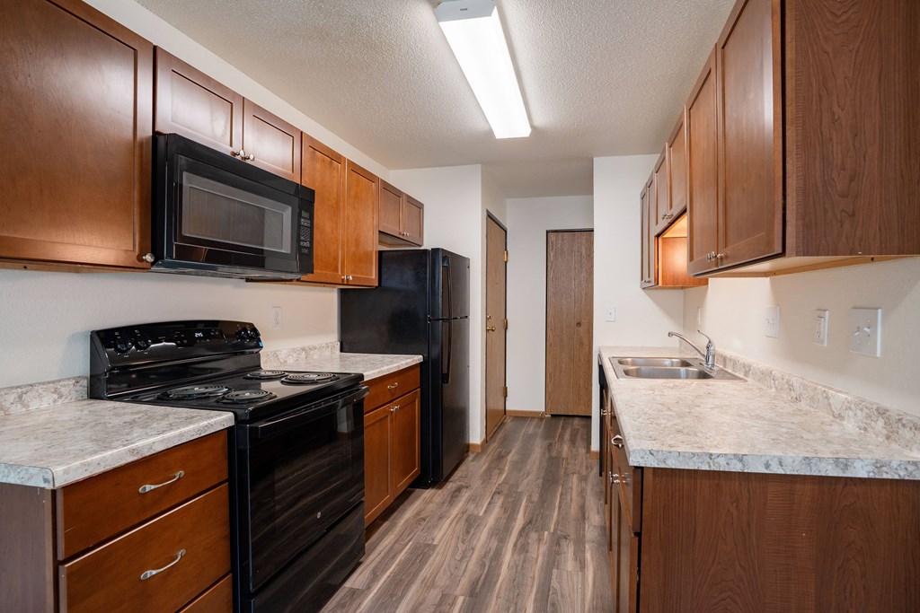 A kitchen with dark wood cabinets and black appliances. Grand Forks, ND Columbia West Apartments