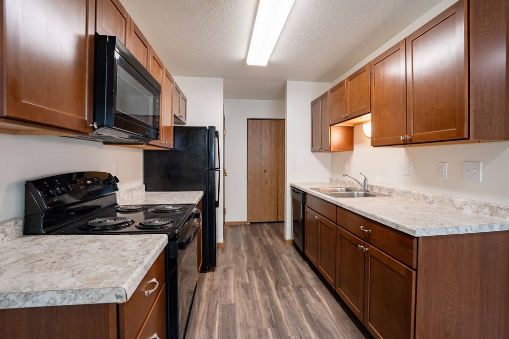A kitchen with dark wood cabinets and a black stove top oven. Grand Forks, ND Columbia West Apartments