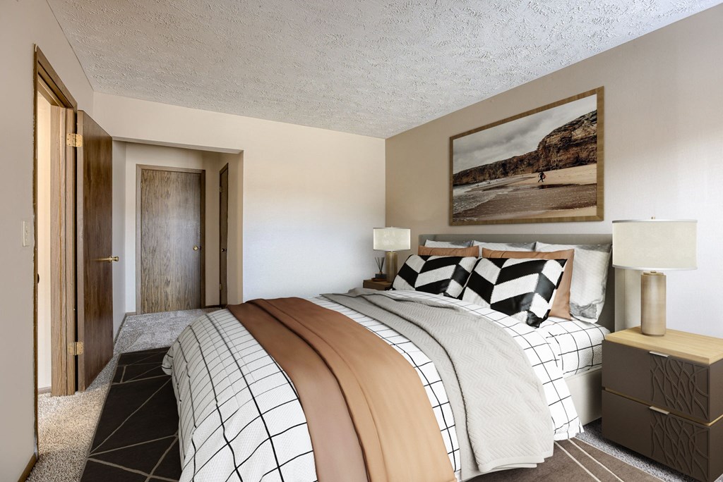 A bedroom with a large bed and a painting on the wall. Omaha, NE Stony Brook Apartments