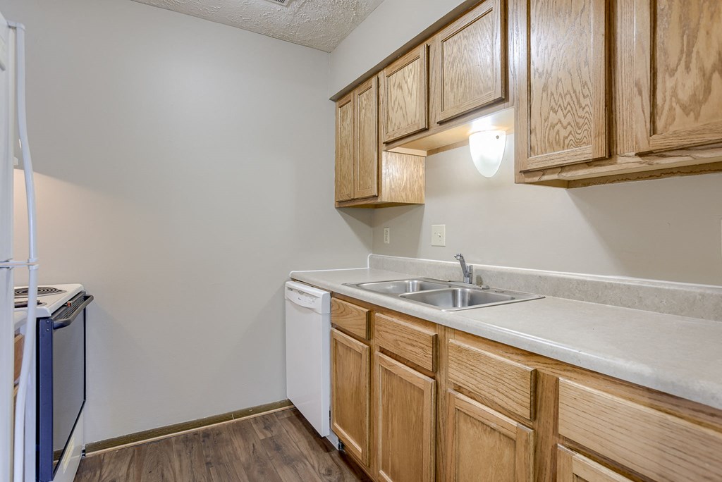 A kitchen with wooden cabinets and a white dishwasher. Omaha, NE Stony Brook Apartments