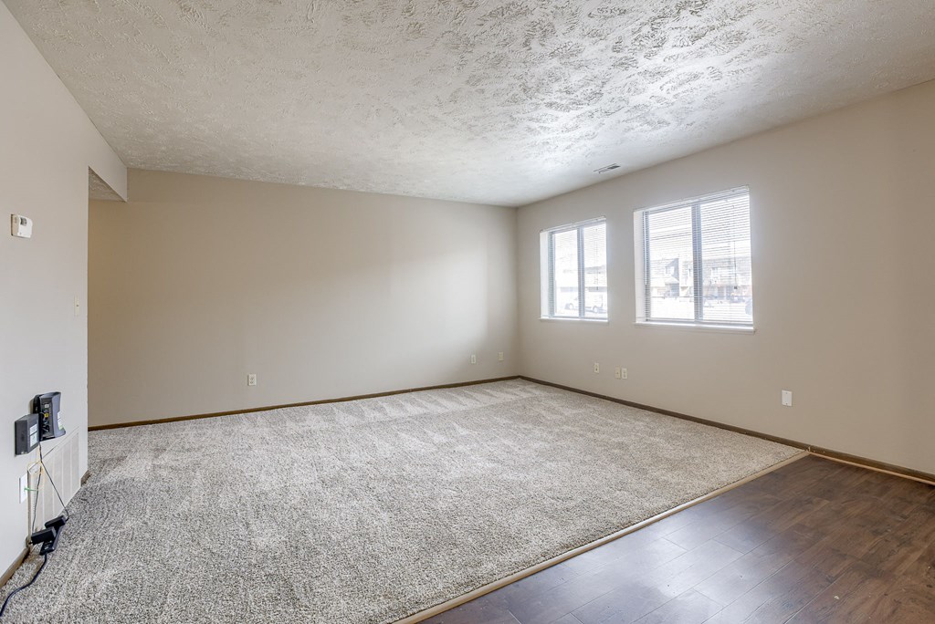 A room with a carpeted floor and two windows. Omaha, NE Stony Brook Apartments