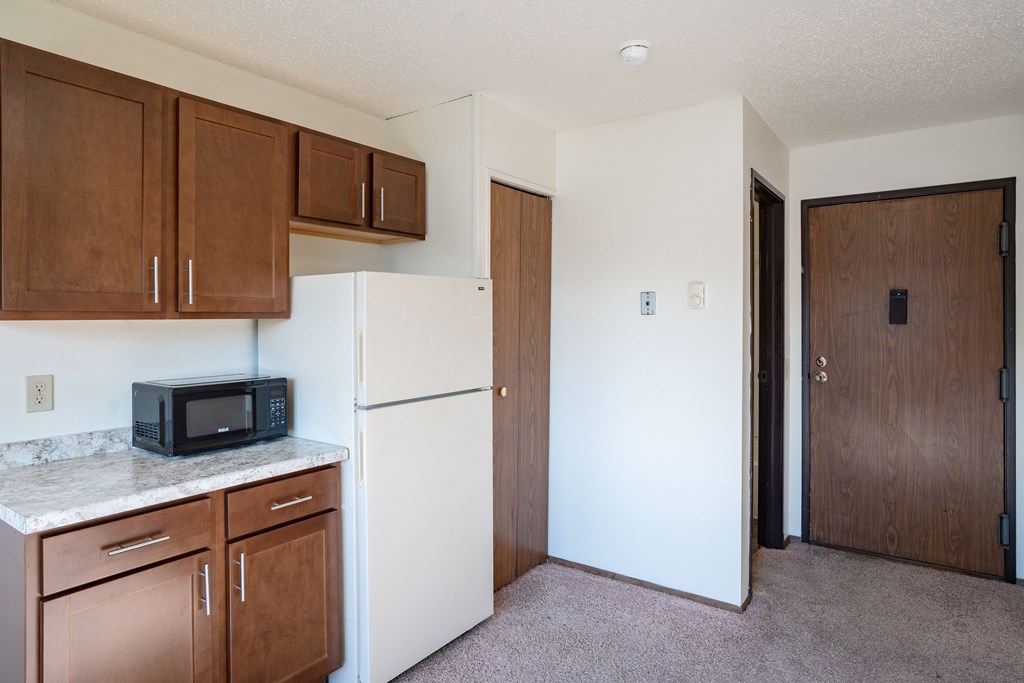 Fargo, ND Pacific Park I Apartments | 01A | Kitchen A kitchen with brown cabinets and a white refrigerator. Fargo, ND Pacific Park I Apartments
