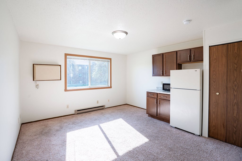A white fridge sits in a kitchen with a window and wooden cabinets. Fargo, ND Pacific Park I Apartments