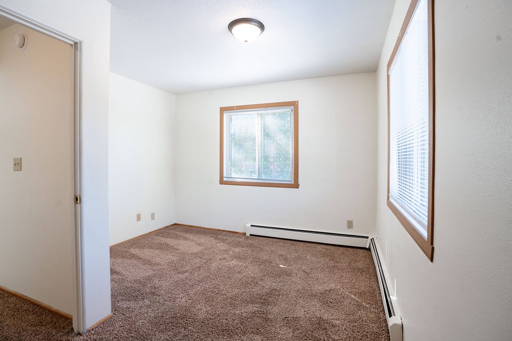 A room with a brown carpet and a window. Fargo, ND Morningside Apartments