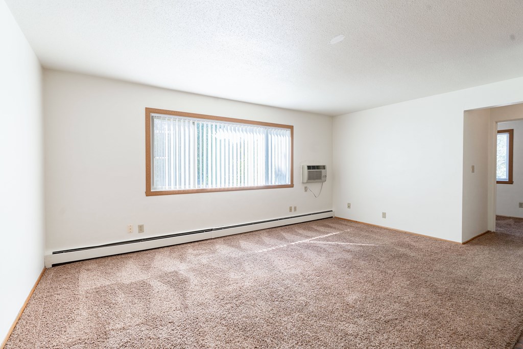 A room with a carpeted floor and a window with blinds. Fargo, ND Morningside Apartments