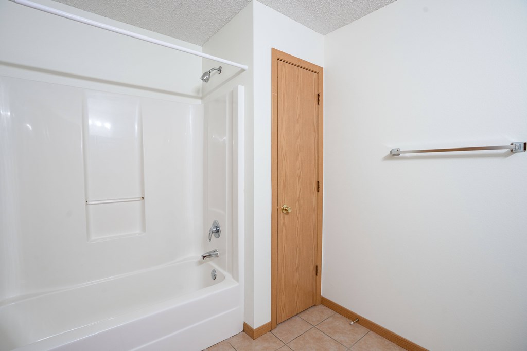 A white bathroom with a wooden door and a white bathtub. Bismarck, ND Sierra Ridge Apartments