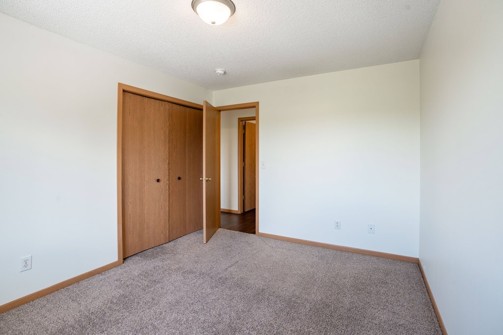 A room with a carpeted floor and two wooden doors. Bismarck, ND Sierra Ridge Apartments