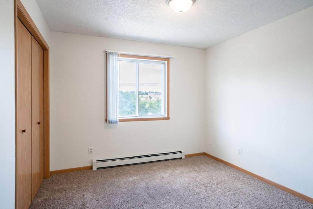 A room with a window and a carpeted floor. Bismarck, ND Sierra Ridge Apartments