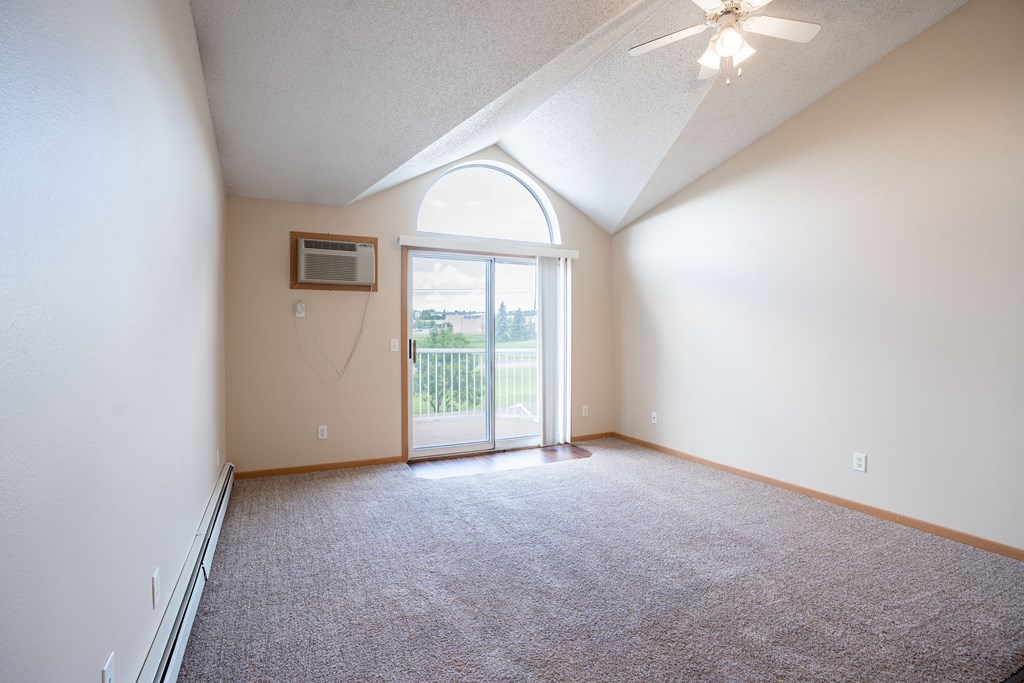 A room with a carpeted floor and a ceiling fan. Bismarck, ND Sierra Ridge Apartments