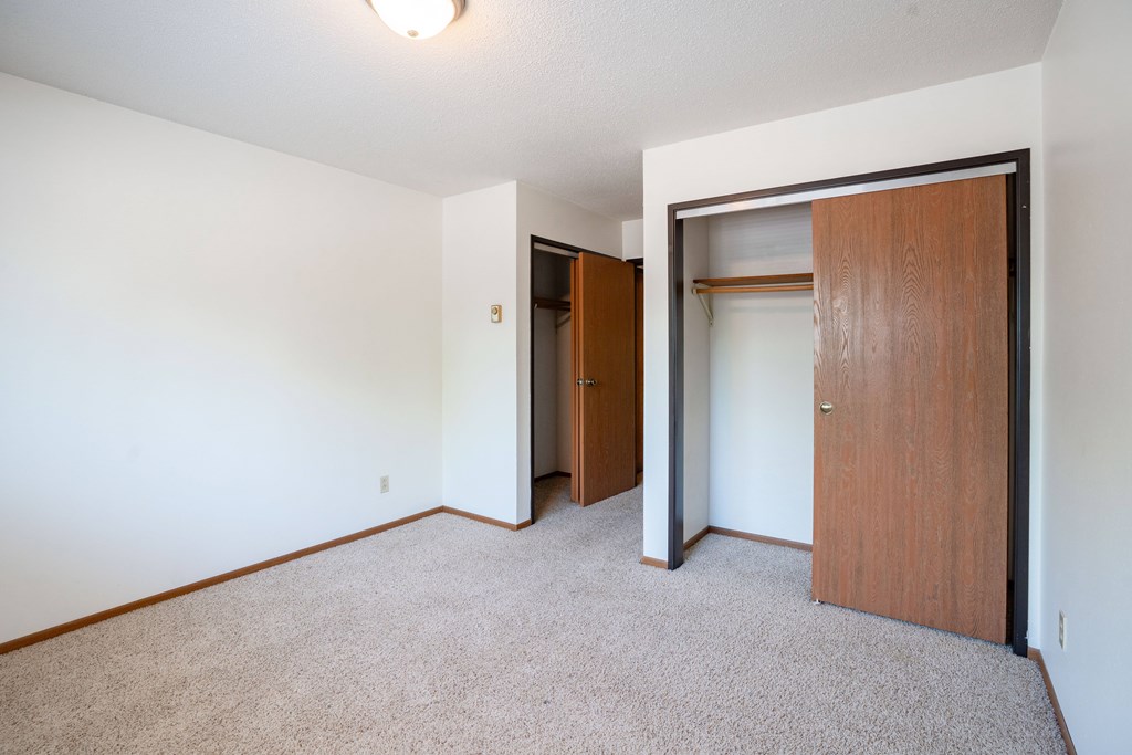 A room with a carpeted floor and a brown door. Fargo, ND West Oak Apartments