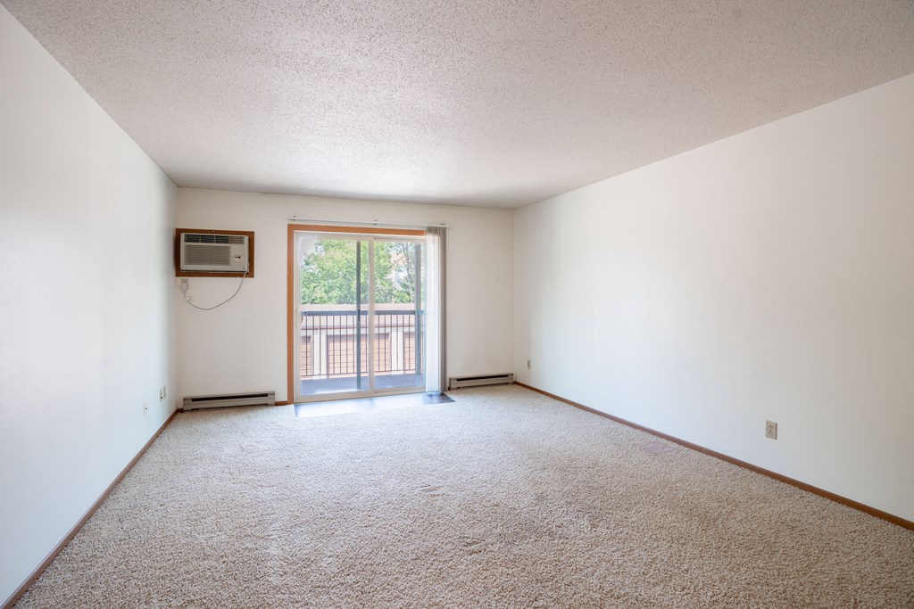 A room with a carpeted floor and a window with a view of a fence. Fargo, ND West Oak Apartments