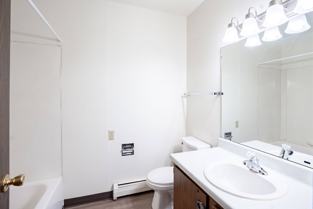 A white bathroom with a toilet, sink, and mirror. West Fargo, ND Parkwest Gardens