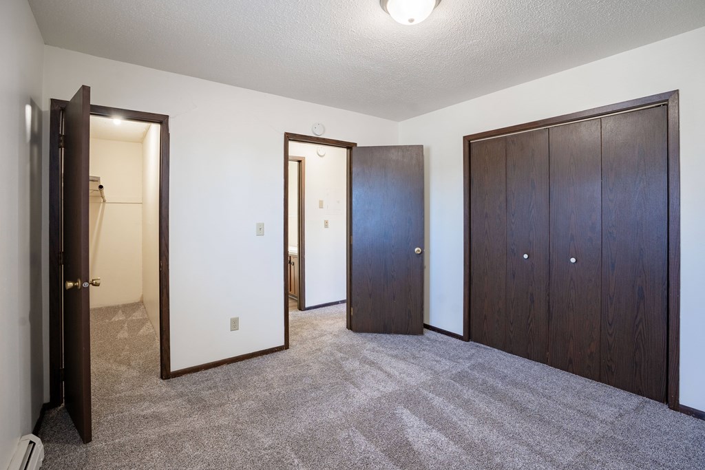 A room with a carpeted floor and three doors. West Fargo, ND Parkwest Gardens
