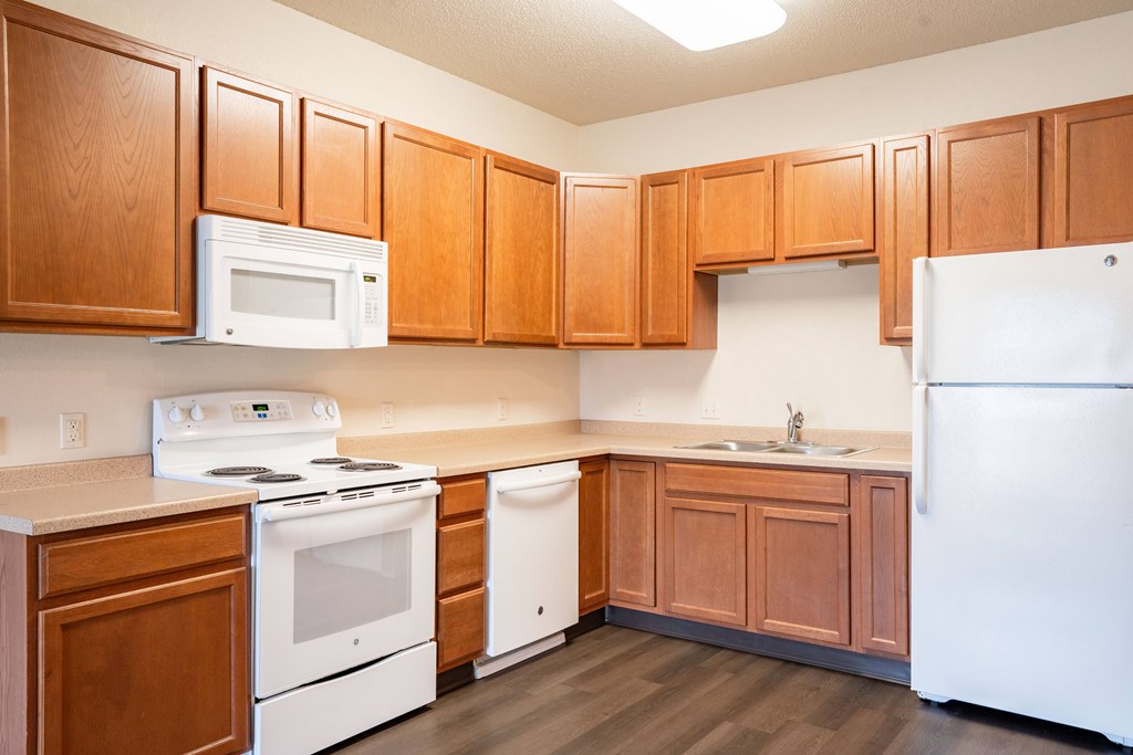 A kitchen with wooden cabinets and white appliances. Fargo, ND North Sky II Apartments