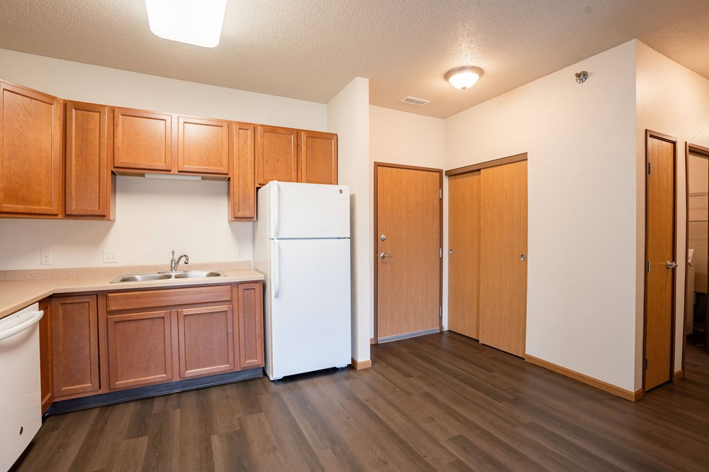 A kitchen with wooden cabinets and a white refrigerator. Fargo, ND North Sky II Apartments